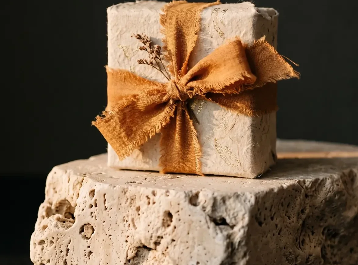 Wide crop of an orange ribbon gift box on a travertine block, dark product photography